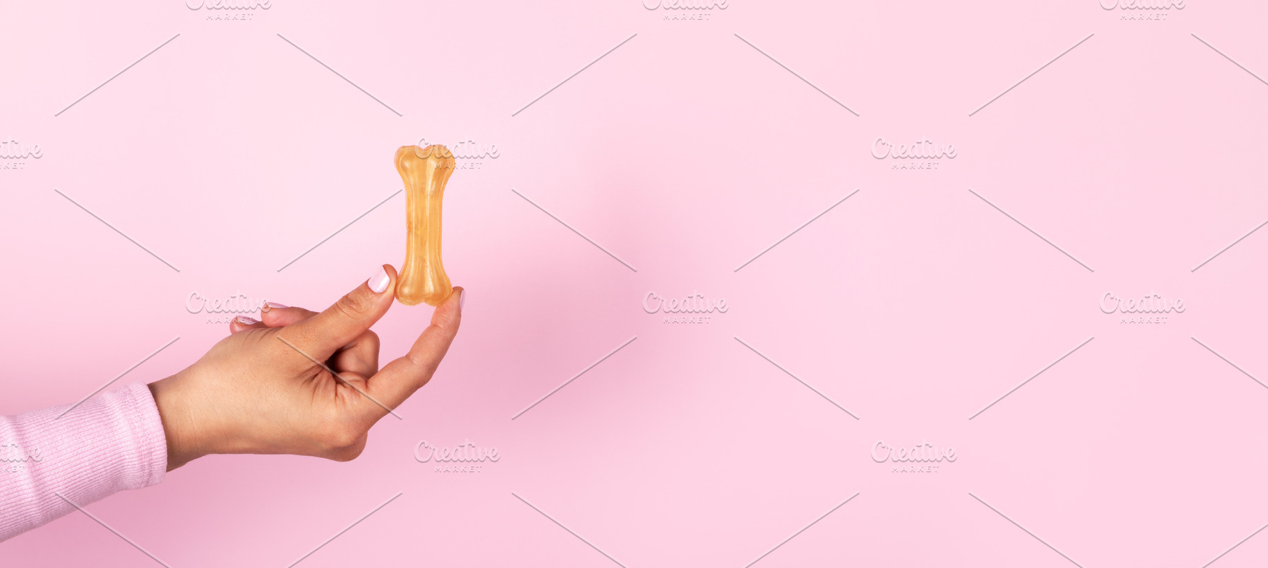 Female hand holding a dog bone treat against a pastel pink backg, a Food & Drink Photo by Ales Munt