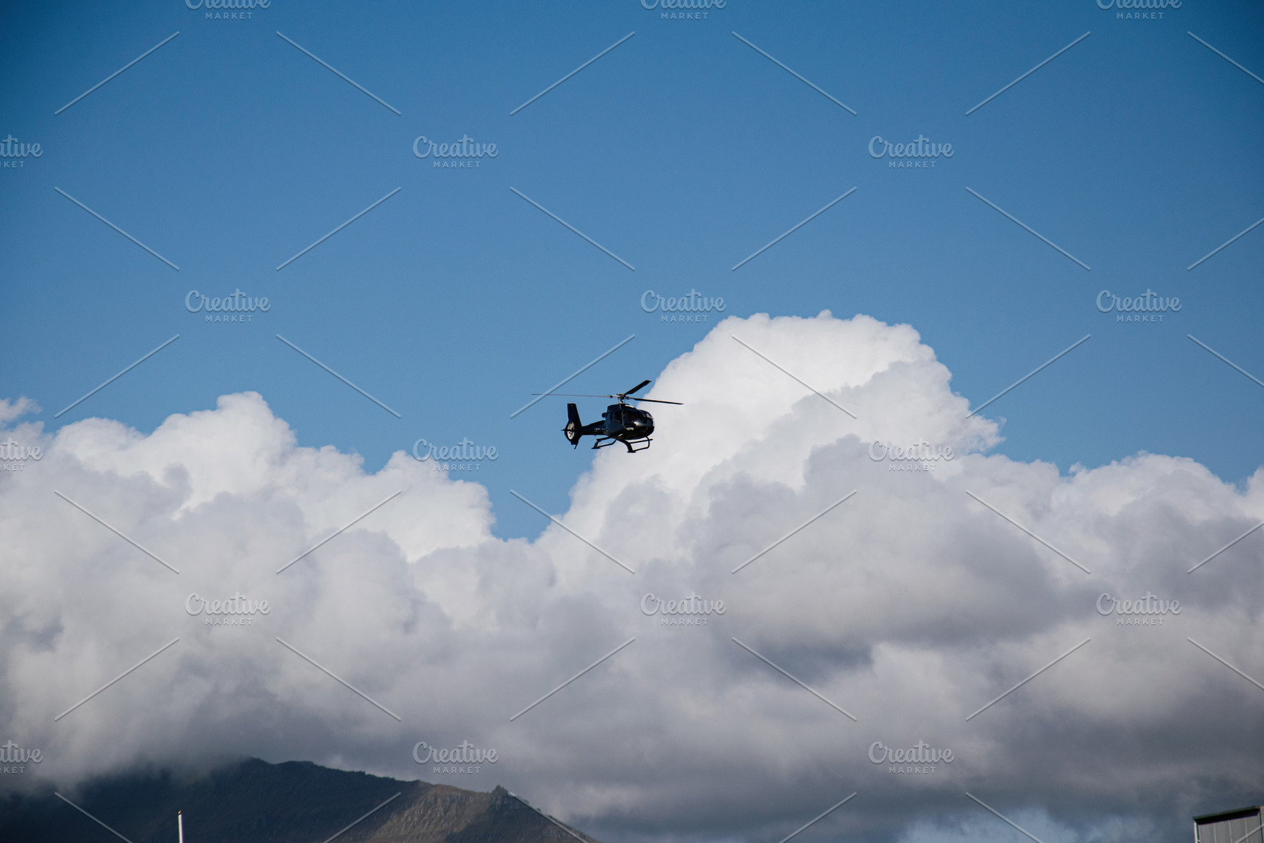 Helicopter flying above mountain with large clouds in Akranes, Iceland, a Photo by AS photostudio