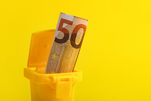 A fifty euro banknote placed in a small yellow trash bin against a vibrant yell, a Business Photo by Ales Munt