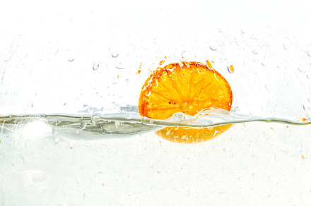 orange halves falling into water on white background.