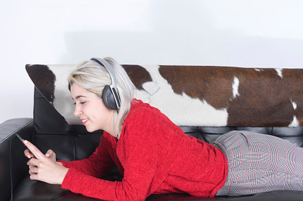 Blonde woman using mobile and listening music by headphones while lying on leat, a Person Photo by 2Design