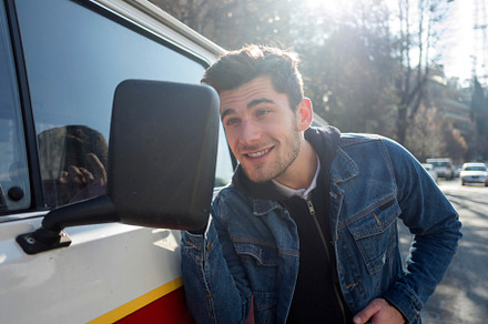 A Young man is pleased to see his handsome looks on the side mirror of a car.