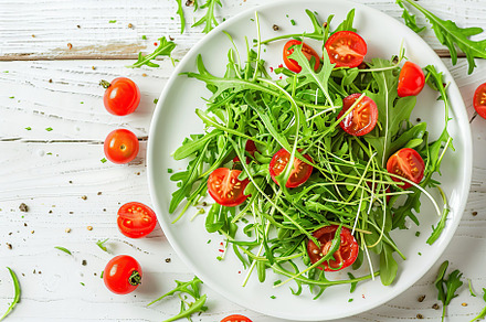 Fresh salad with microgreen, arugula and tomatoes in plate on wooden table, a Food & Drink Photo by AlyaAnd