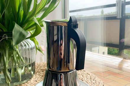 A moka pot and tulips on a woven stool near a bright window.