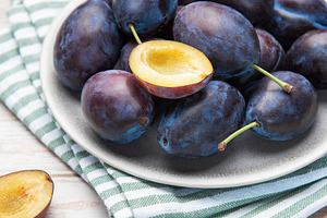 Fresh ripe plums in grey bowl on wood table, a Food & Drink Photo by Olena Rudo