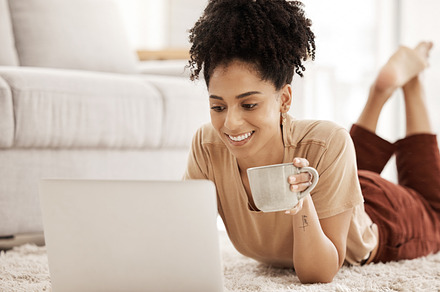 Laptop, coffee and relax with a woman lying on the floor in her home living room over the weekend. Computer, social media and internet with a female typing or reading an email while in her house, a Photo by Peopleimages.com