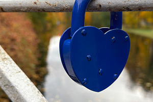 A blue heart-shaped padlock attached to a metal railing on a bridge, with a riv, an Industrial Photo by Textures & Backgrounds