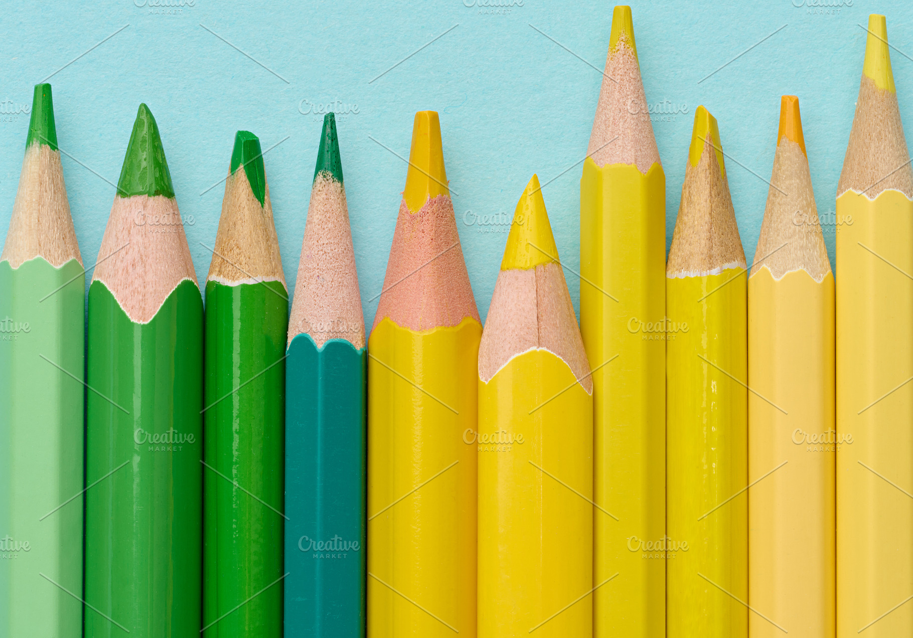 Close-up of a row of green and yellow wooden pencils on a blue b, a School & Education Photo by ndanko