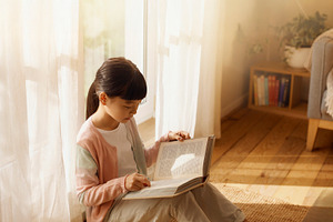 Asian girl sitting on the floor near a bright window, holding an, a School & Education Photo by DanFLCreativo