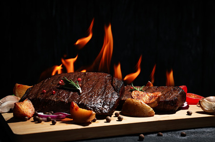Concept of tasty food with beef steaks on dark wooden table, a Food & Drink Photo by AtlasStudio