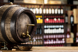 Wine barrel with copper tap and bottles of wine on the shelves a, a Food & Drink Photo by Volff