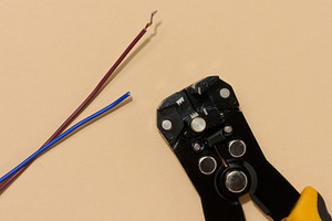 Wire stripper lies next to two cut electrical wires red and blue, a Technology Photo by ndanko