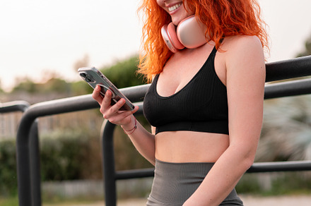 Young woman with red hair checks phone while exercising outdoors in fitness gea