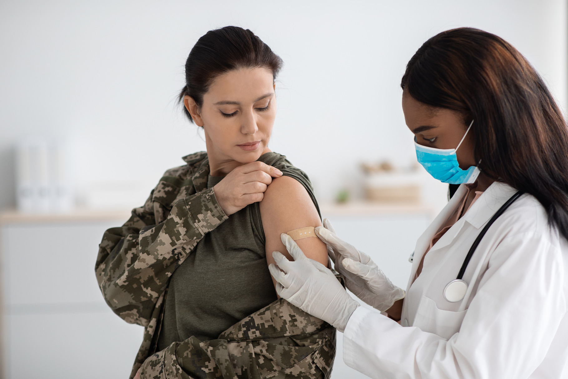 Black Female Doctor Applying Plaster On Soldier Woman's Shoulder After ...