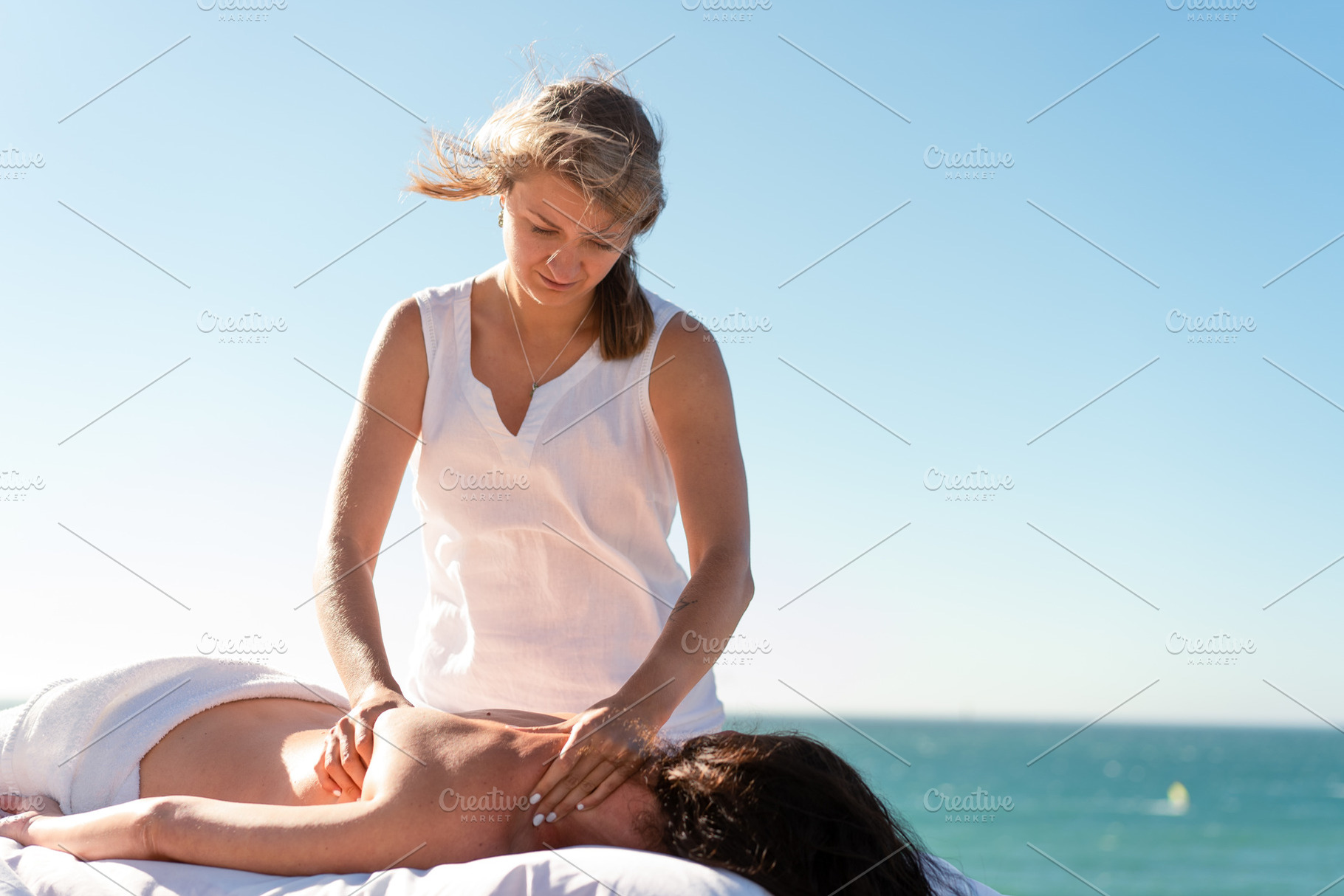 Therapist massaging woman's naked back against sea and clear blue sky, a Person Photo by andreonegin market