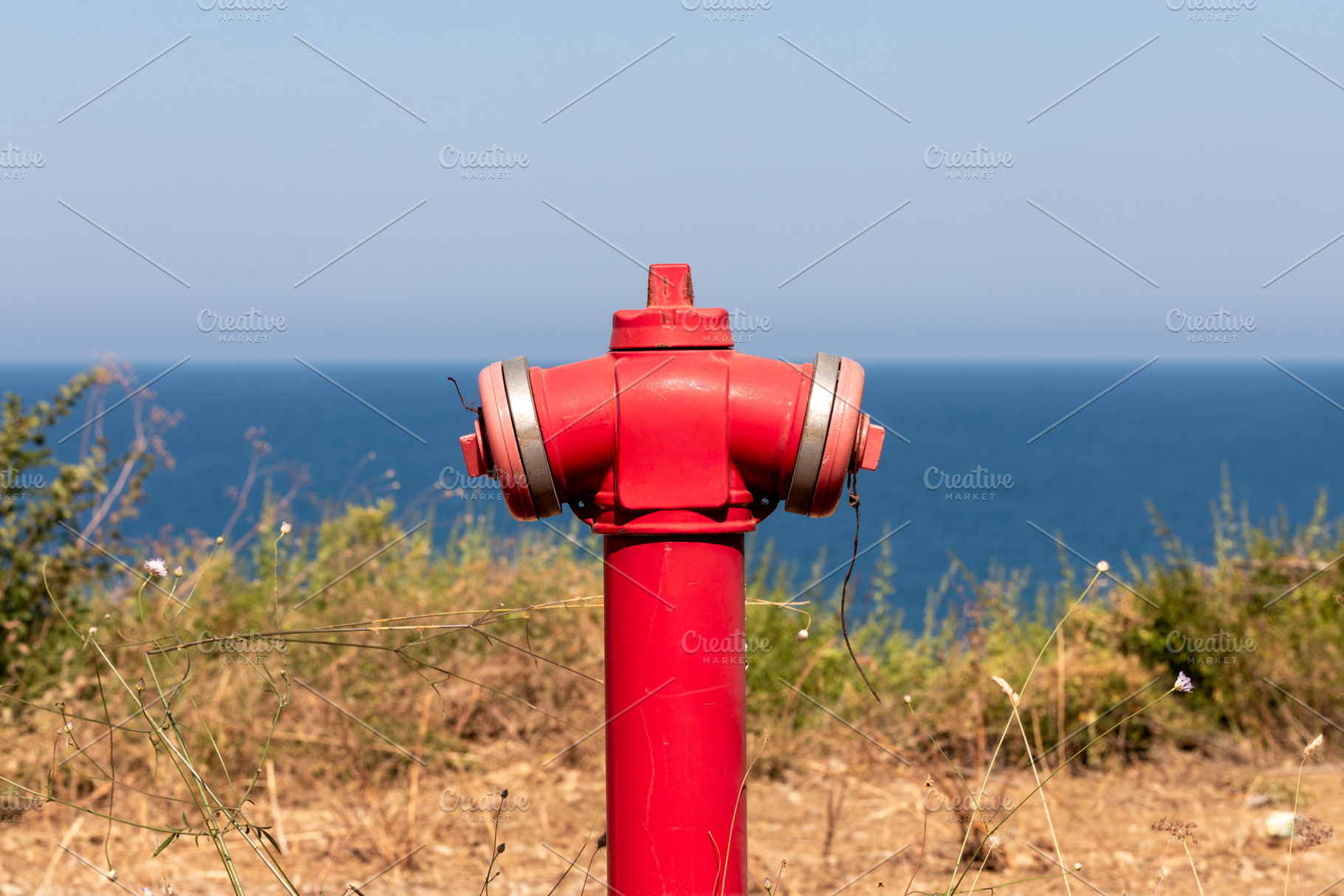 Bright red fire hydrant standing against a clear blue sky and calm ocean, surro, a Technology Photo by Ales Munt