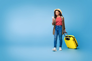 Young black woman with smartphone booking hotel or plane tickets online, walkin, a Photo by Prostock-Studio