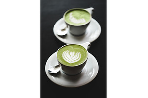 Two cups of matcha latte on black
