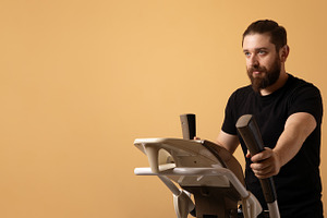 Bearded man in black t-shirt using elliptical machine against pl, a Person Photo by Ales Munt