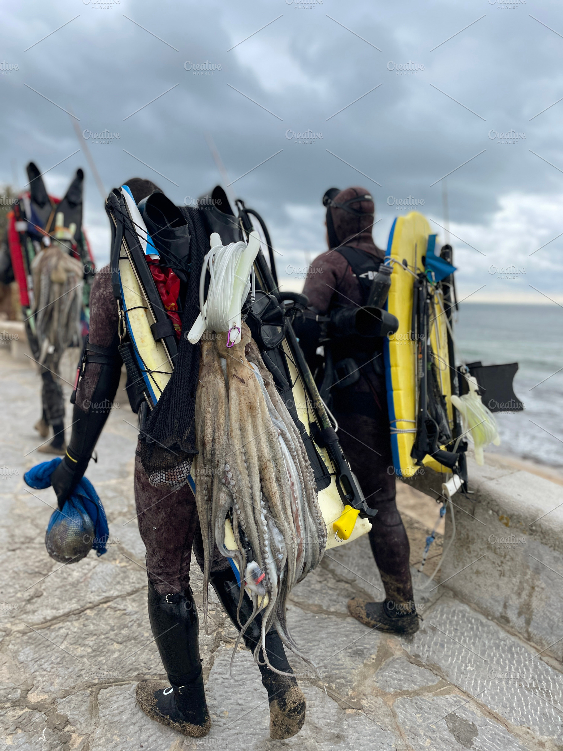 Anonymous spear fishers with their catch and equipment on coastline, a Photo by andreonegin market