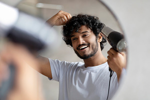 Excited indian man using hairdryer after shower, drying his curly hair, making, a Person Photo by Prostock-Studio