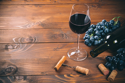 Bottle and glass of red wine grape corkscrew and cork on wooden background