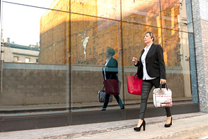 Businesswoman walking by glass wall with reflection, a Photo by RF Images