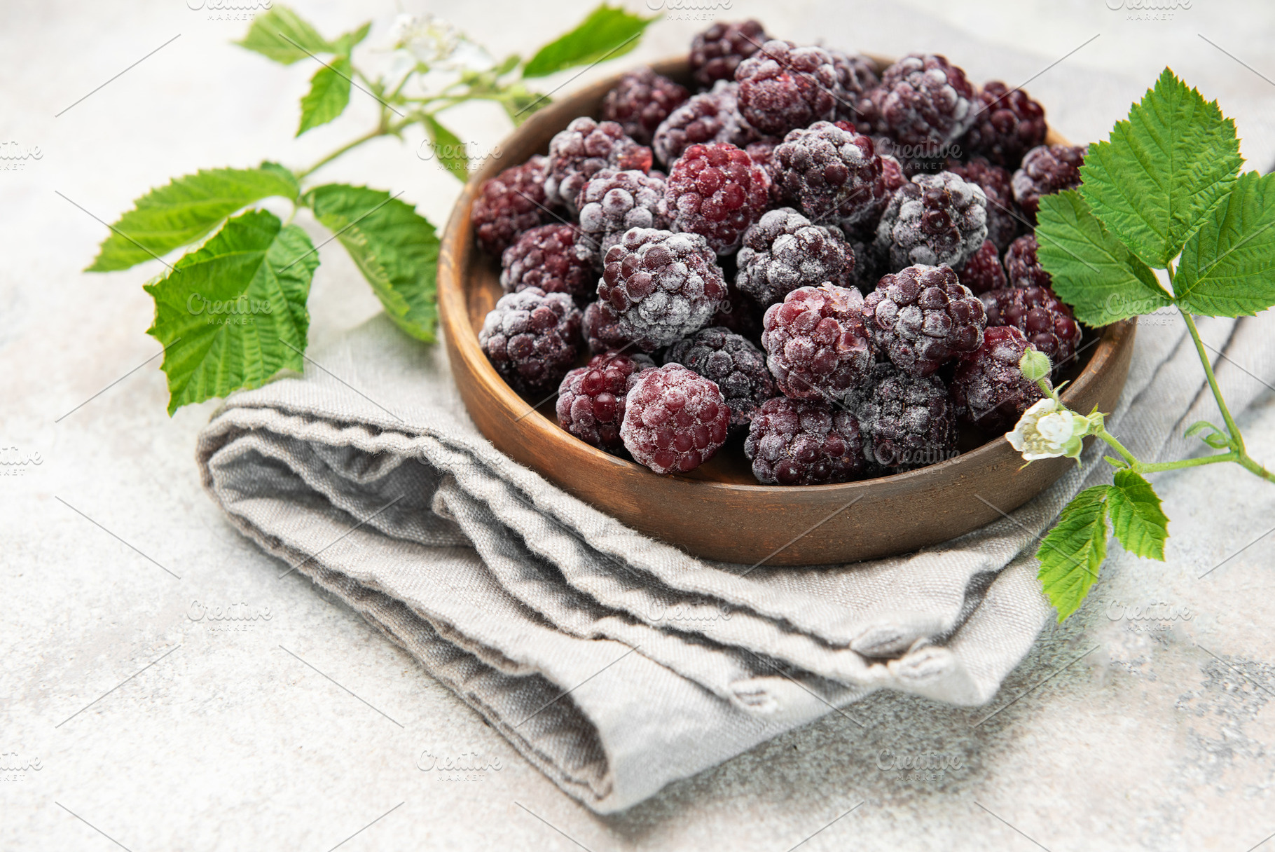 Frozen blackberries with green leaves in wooden bowl, a Food & Drink Photo by Olena Rudo