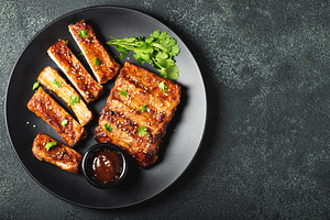 Hot grilled spare ribs from a summer BBQ served on a plate with sauce. Top view, a Food & Drink Photo by Budarinphoto
