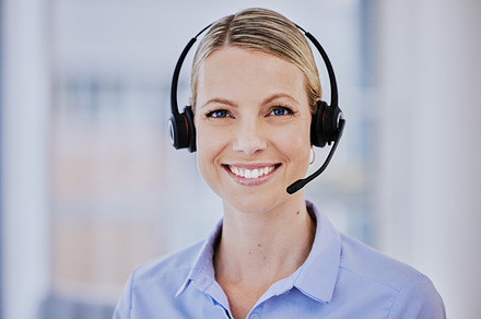 Smiling young caucasian female call centre agent talking on headset while working in an office. Confident and happy businesswoman consulting and operating a helpdesk for customer sales and service support, a Photo by Peopleimages.com