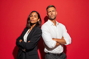 Confident business professionals posing against a vibrant red background, a Photo by AlyaAnd
