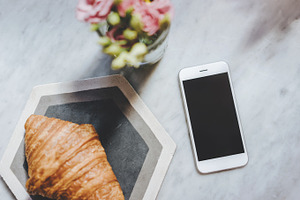 Phone with croissant and flowers