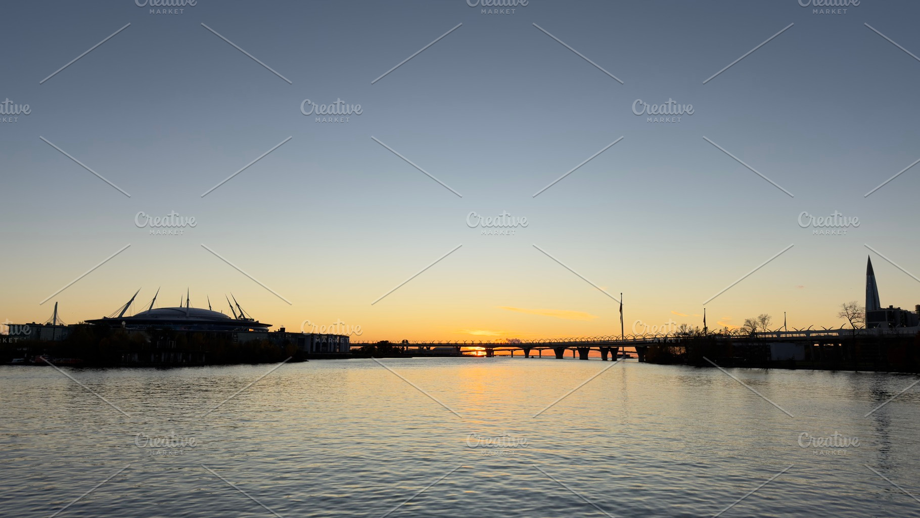 A serene sunset over a river, with silhouettes of buildings and a bridge in the, a Nature Photo by Textures & Backgrounds