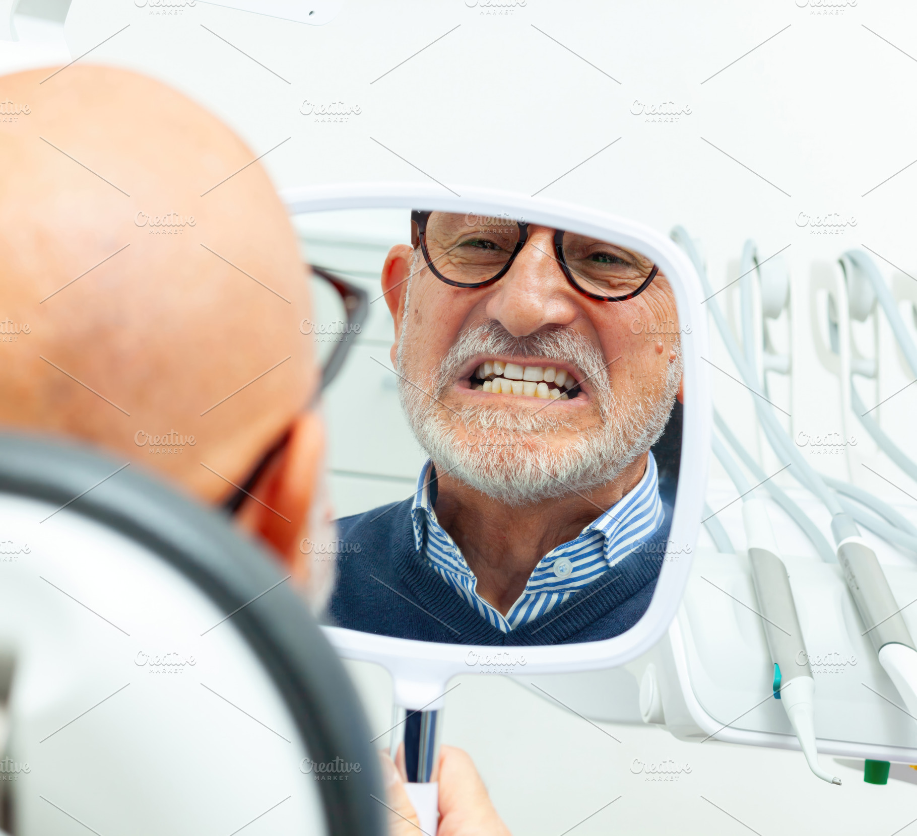 Senior man checking his teeth in the mirror at the dentist's office, a Health & Medical Photo by Antonio Gravante Market