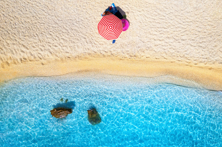 Aerial view of red umbrella, sandy beach, blue sea at sunset, a Nature Photo by den-belitsky
