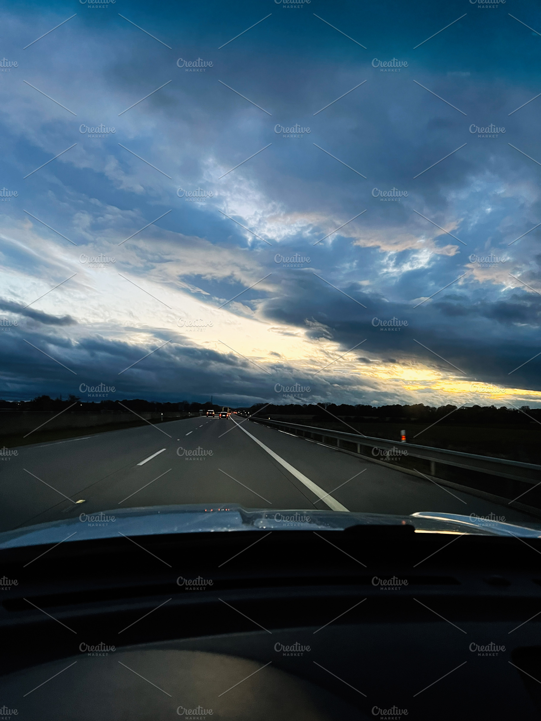 Driving on an empty highway at dusk under dramatic blue skies and glowing horiz, a Photo by AS photostudio