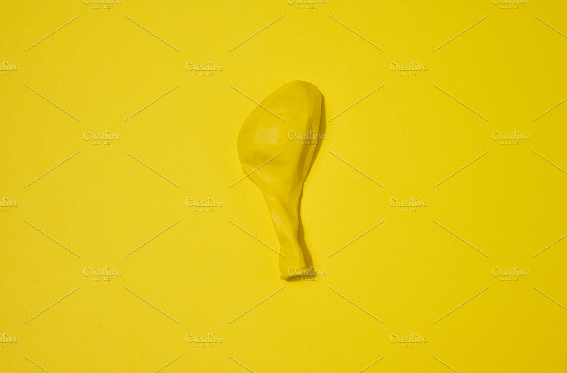 One yellow deflated balloon lies on a yellow background, an Abstract Photo by ndanko