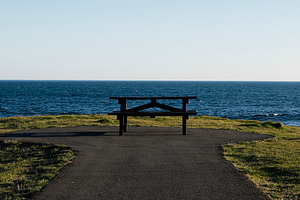 Scenic coastline with bench overlooking waves in Akranes, Iceland under clear s, a Photo by AS photostudio