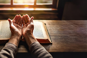 Person praying with open hands above a book