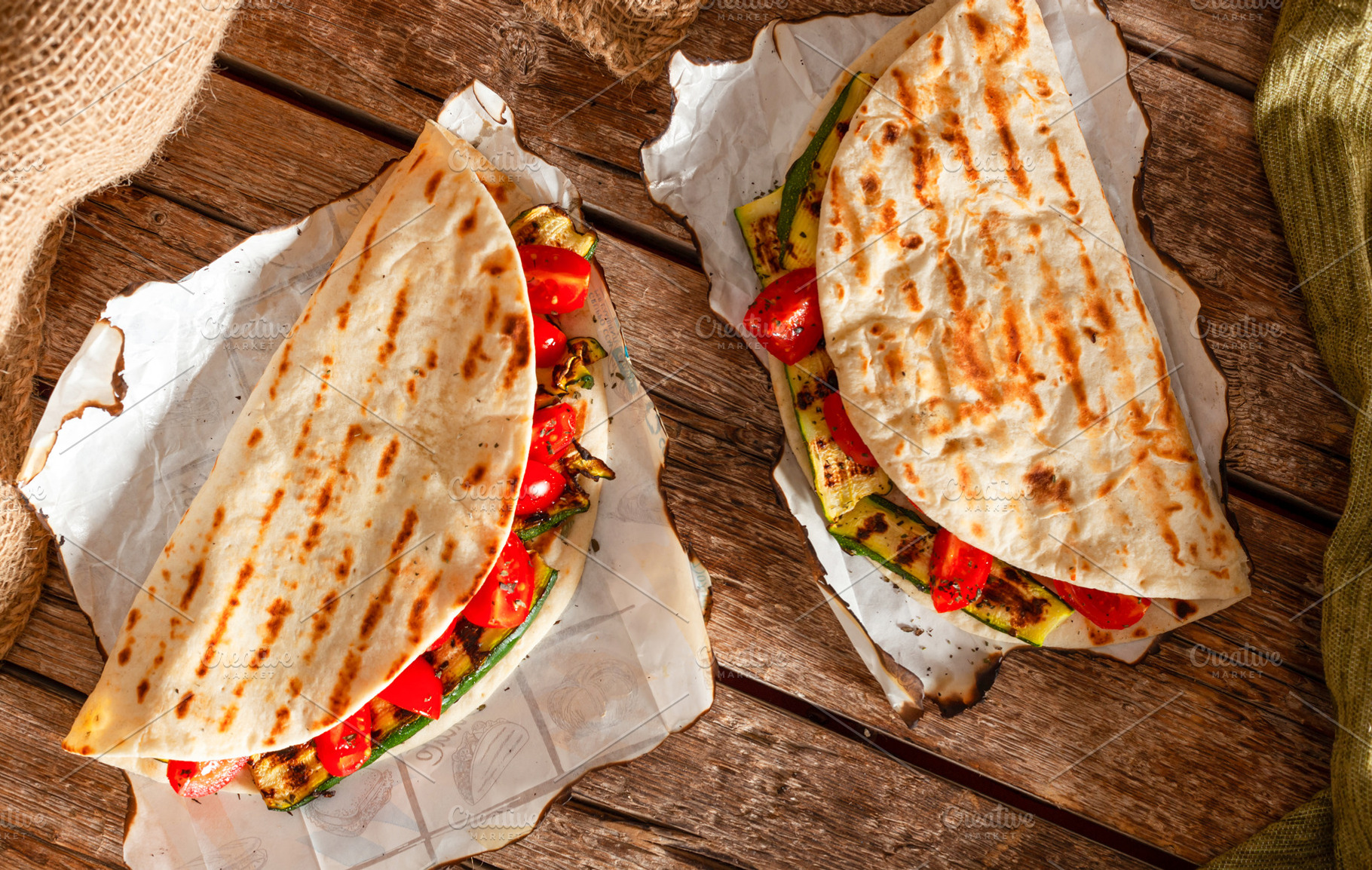 Two piadine with grilled zucchini and tomatoes resting on baking paper sheets, a Food & Drink Photo by Antonio Gravante Market