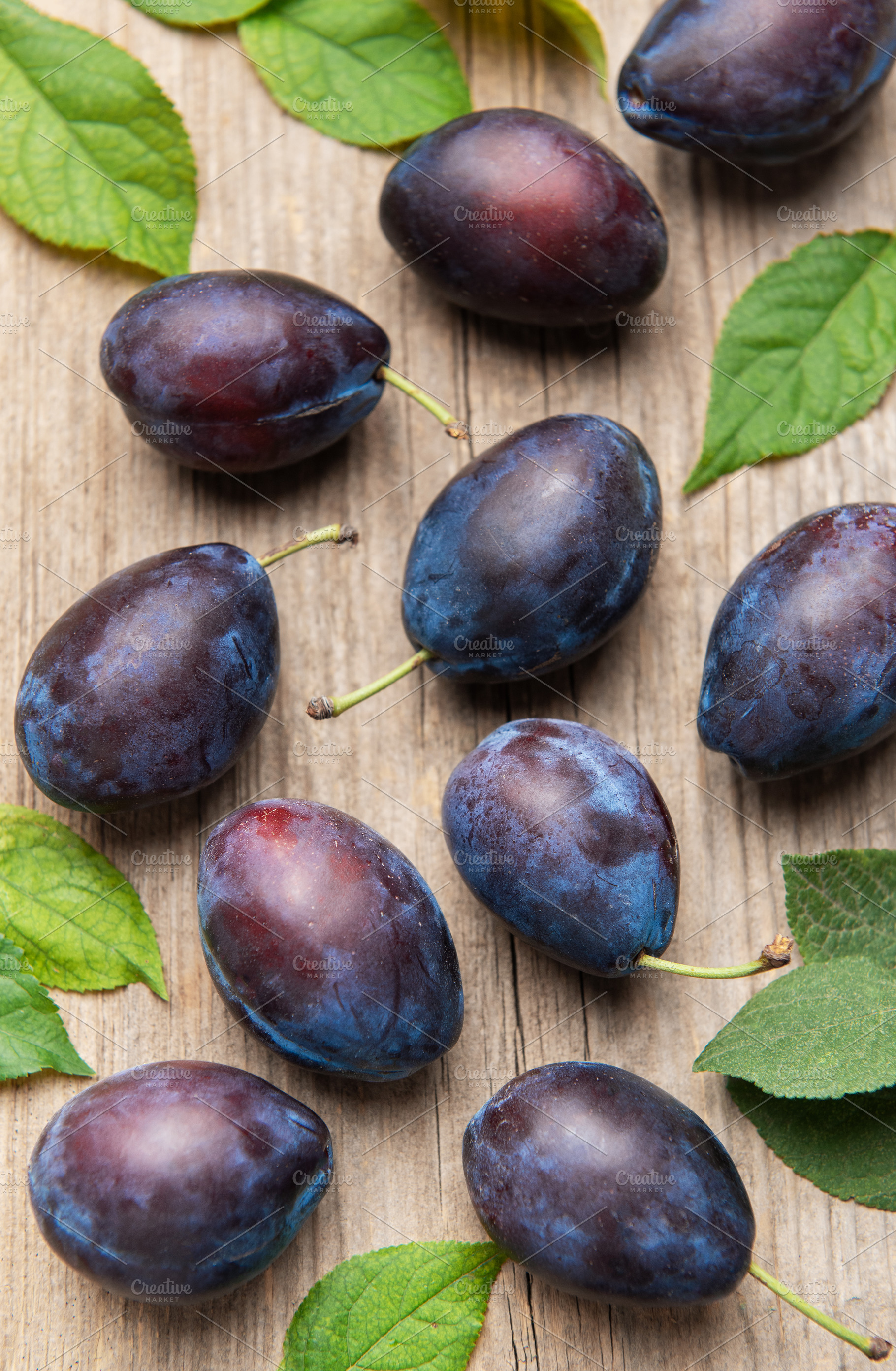 Ripe purple plums fallen on wooden table, a Food & Drink Photo by Olena Rudo