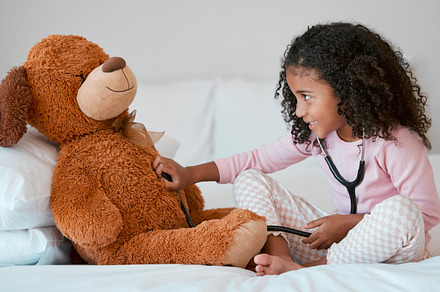 Teddy bear, learning and child with stethoscope for healthcare, heart and anatomy education in her bedroom and home for development. Girl play with hospital, doctor or nurse cardiology toys or tools, a Photo by Peopleimages.com