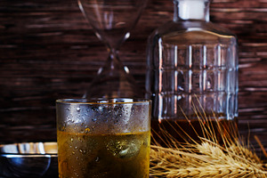 Glass of whiskey with ice an ashtray and a decanter containing whiskey