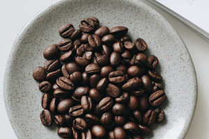 Coffee beans on white plate, a Photo by Virgo Studio
