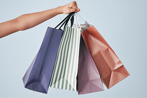 Hands, shopping bags and purchase on mockup in sale, discount or fashion against a gray studio background. Hand of shopper holding bag of gifts, present or luxury retail products on copy space, a Photo by Peopleimages.com