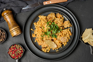 Pilaf with rice and pieces of meat in a black round plate on the, a Food & Drink Photo by ndanko