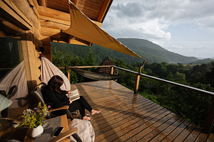 Woman reading on a cozy wooden terrace with scenic mountain views, a Photo by AS photostudio