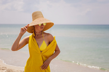 young fashionable woman in a yellow hat dress and sun glasses is posing on beac, a Person Photo by SaulichPhoto