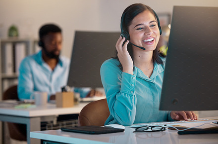 One happy young caucasian call centre telemarketing agent talking on a headset while working on a computer in an office. Confident and friendly businesswoman consultant operating a helpdesk for customer service and sales support, a Photo by Peopleimages.com
