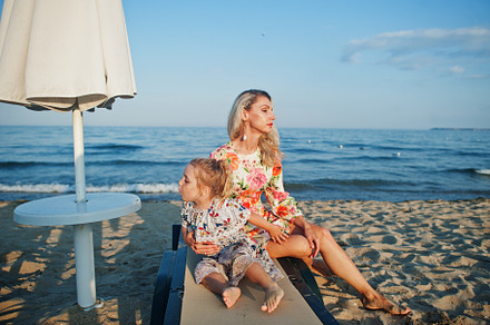 Mother and beautiful daughter having fun on the beach, sitting o, a Person Photo by AS photostudio